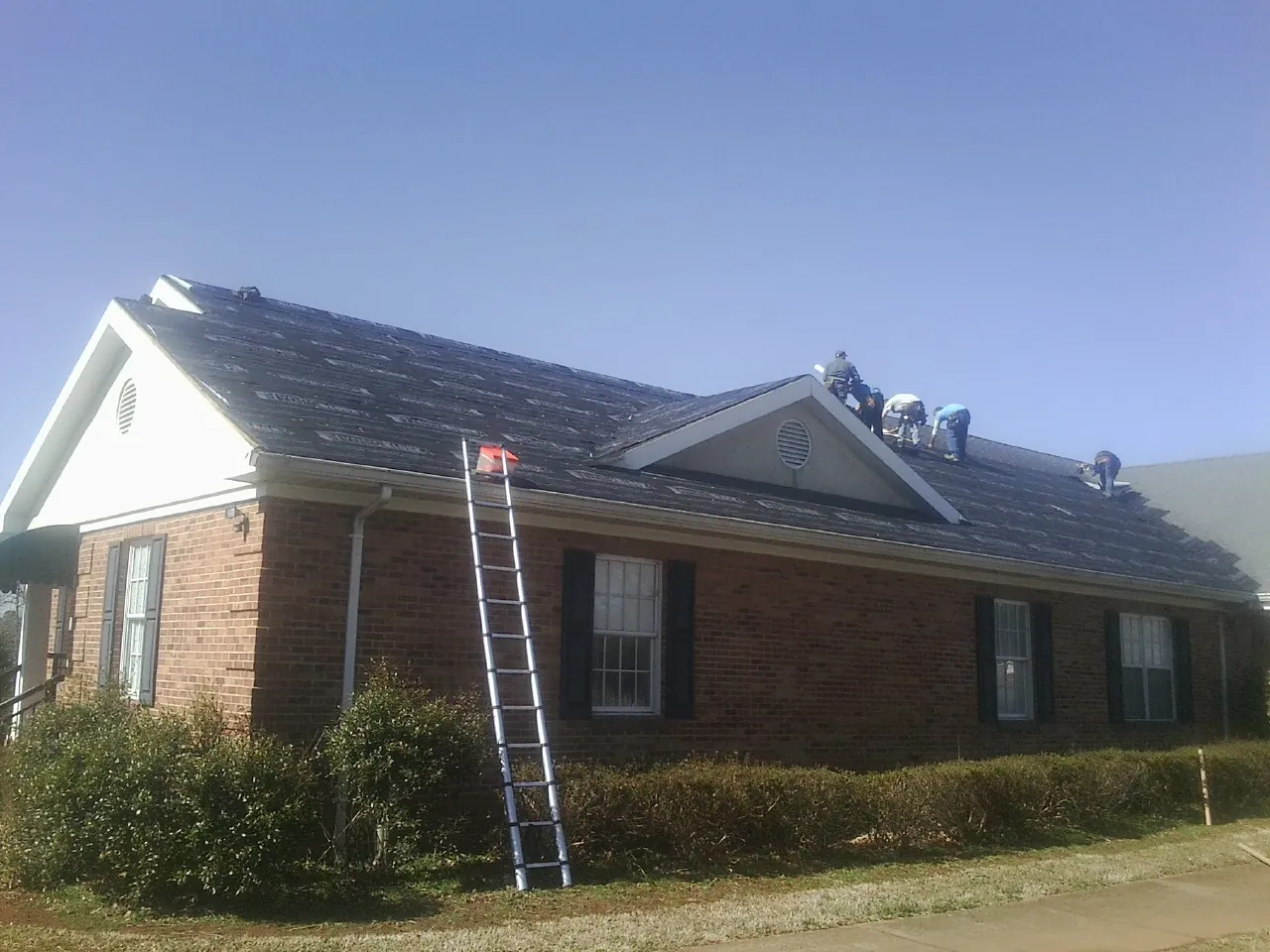 Crew tearing shingles off a brick ranch roof with a ladder set — Emergency Roof Repair work by our crew in Adah