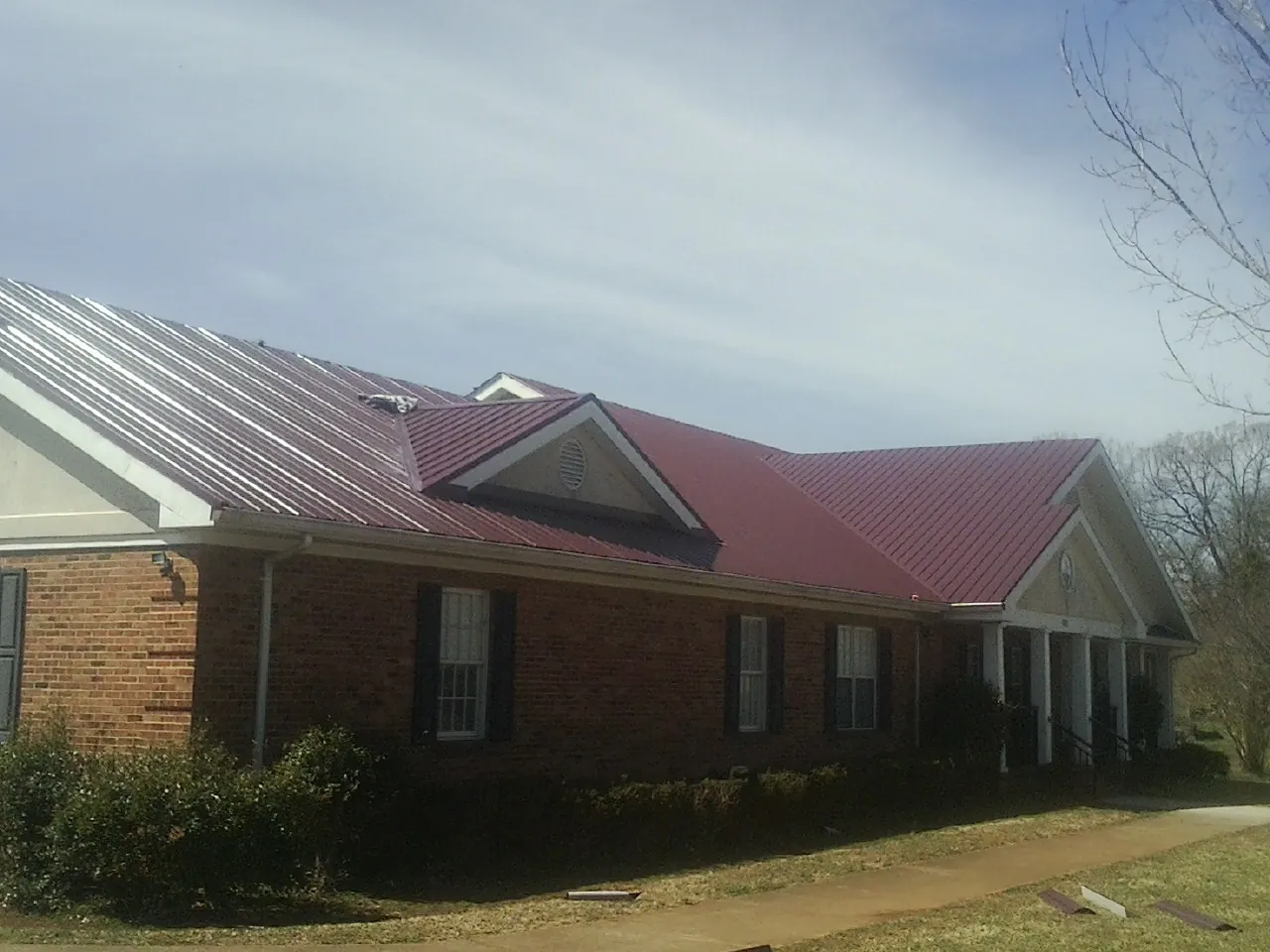 Red metal roof with gabled entries on a long brick building in Adah