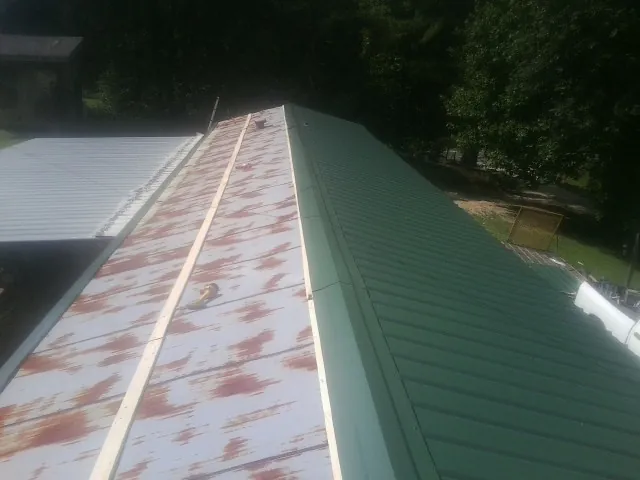 Old rusted panels beside newly installed green metal roofing — Wind Damage Roof Repair by Roofing Brothers in Adah