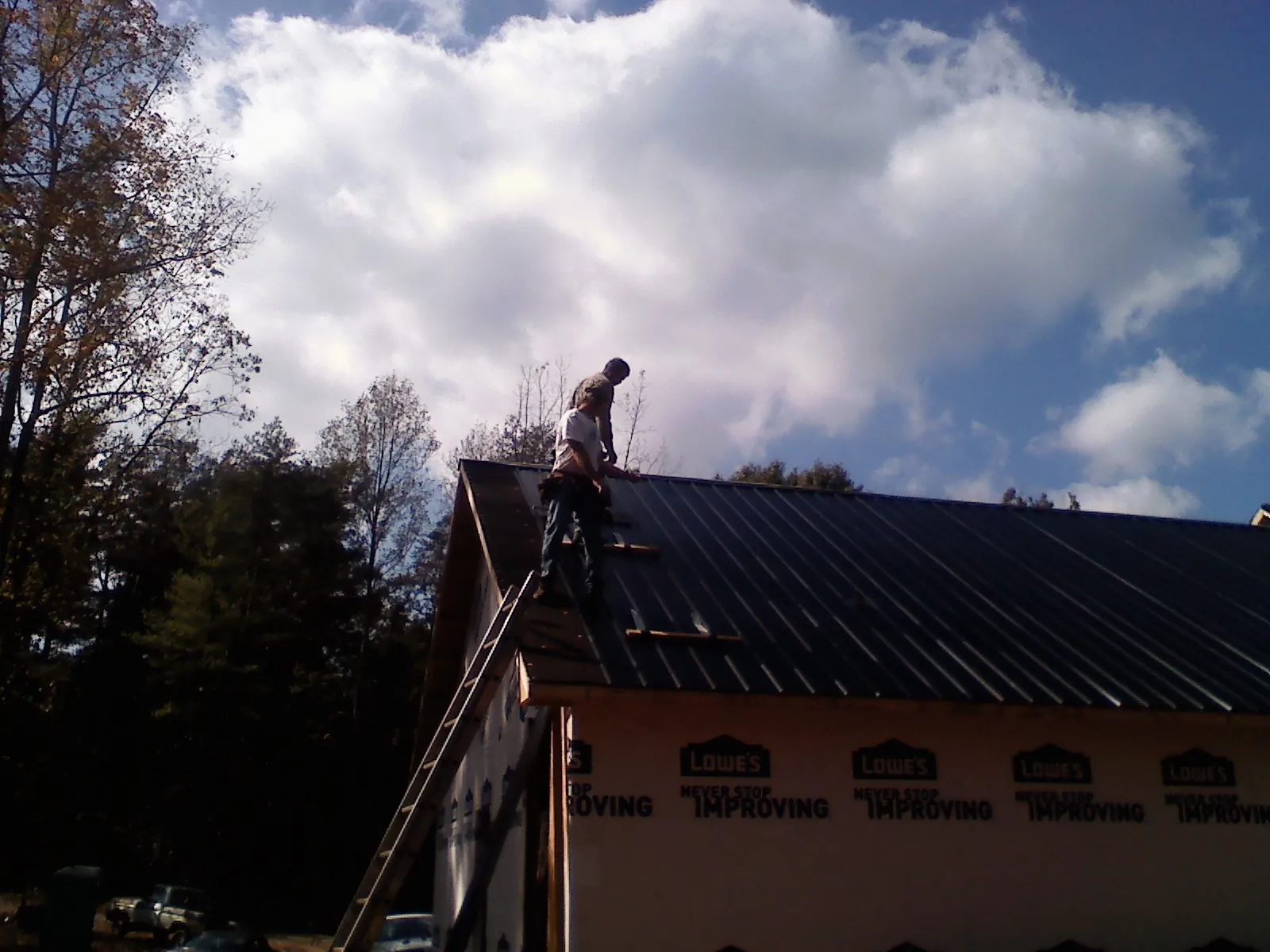 Roofer fastening dark metal panels high against a cloudy sky, from a Roof Inspection job in Adah