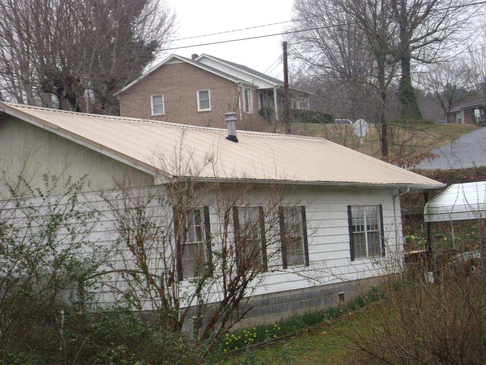 Tan metal roof on a white sided house set into a hillside — Commercial Roofing by Roofing Brothers in Adah